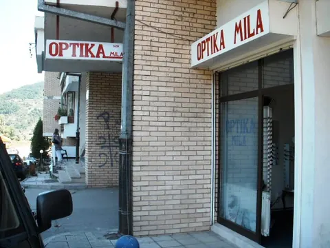 Ulaz u Optiku Mila u Foči — natpis iznad vrata na zgradi od žute cigle